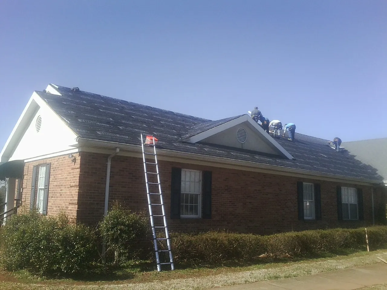 Crew tearing shingles off a brick ranch roof with a ladder set — Metal Roof Repair work by our crew in Edna