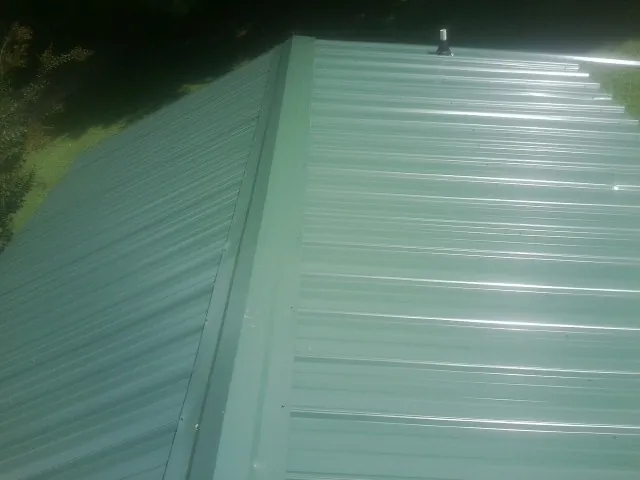 New green metal panels meeting at the ridge of a roof — Flat Roof Repair work by our crew in Edna